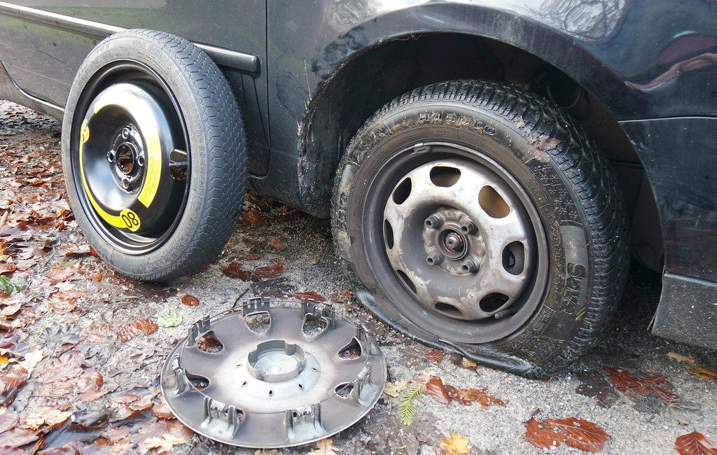 Flat tire on a car next to a spare wheel and a removed hubcap during a roadside tire change